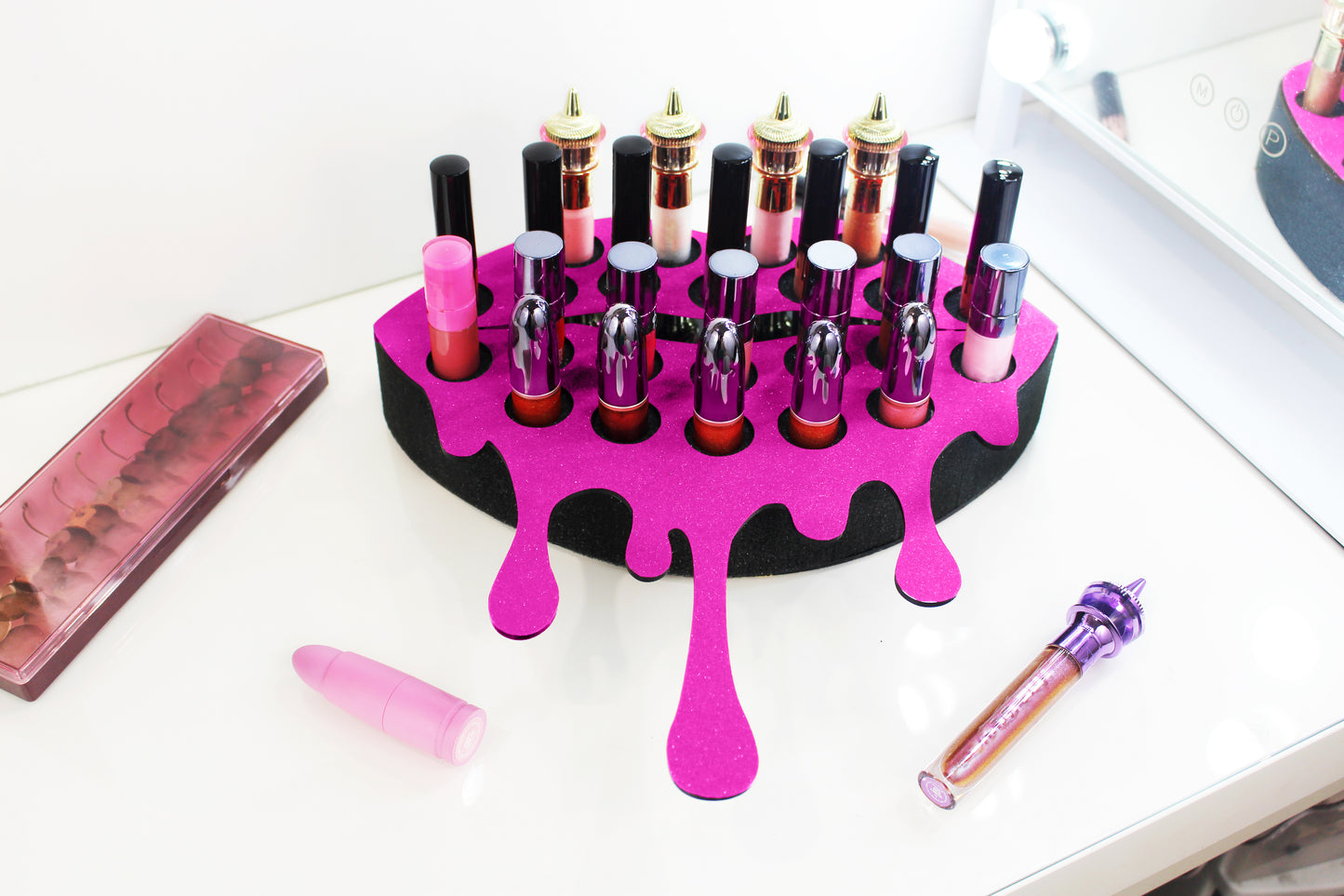 Dark Pink Medium Lip Design Lipstick Organizer holding 23 lipsticks mounted on the wall, keeping lipstick organized and easy to reach. This wall mounted makeup organizer looks like art on the wall of your bathroom or makeup room. Shown being used to organize makeup sitting on a makeup vanity.