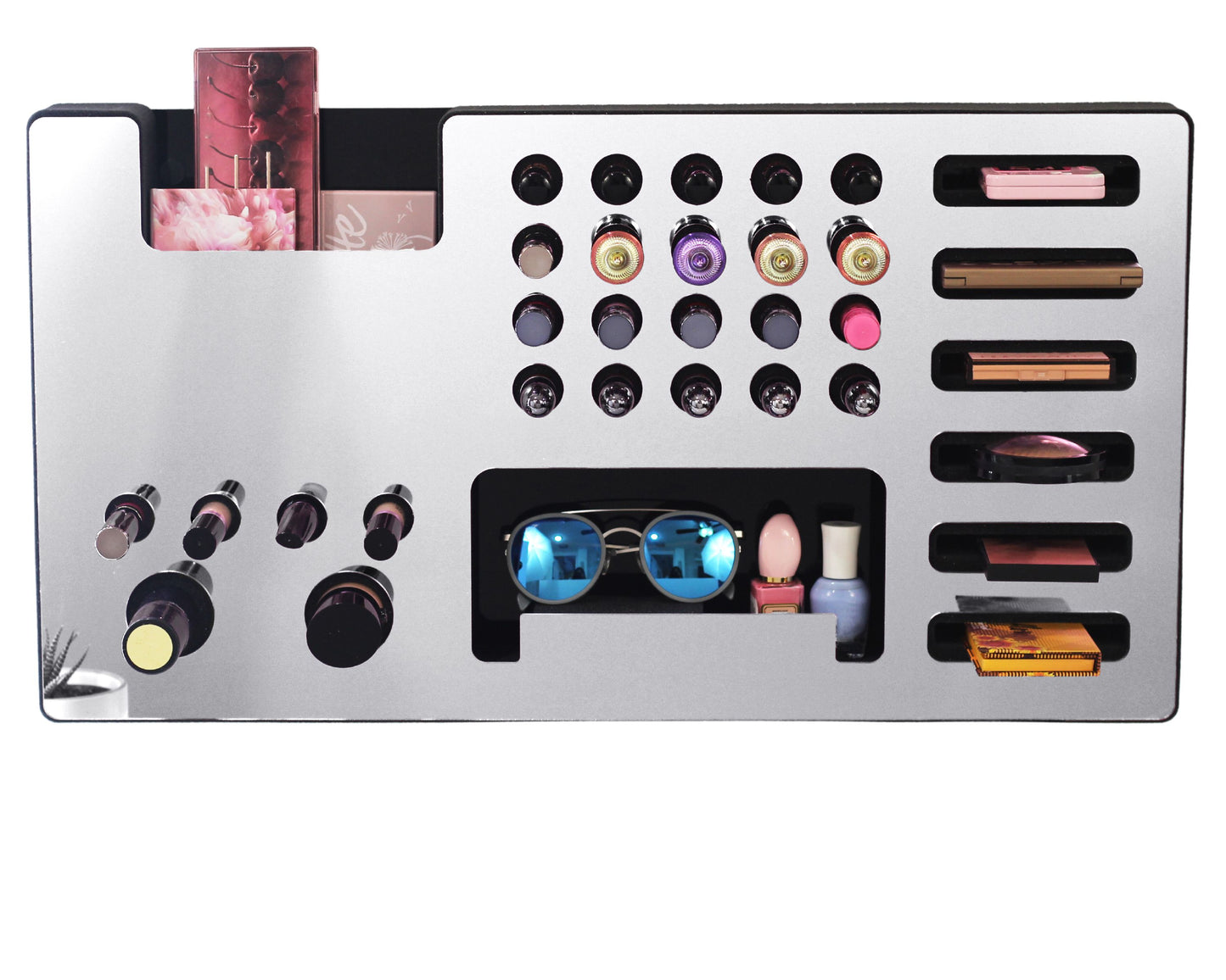 Mirror Silver Ultra Complete Makeup Solution Organizer shown mounted on the wall holding lipsticks, lip glosses, nail polishes, brushes, sunglasses and more by keeping items accessible and off of the counter. Shown next to a makeup vanity with samples of suggested items the organizer can hold. Shown with a white background.