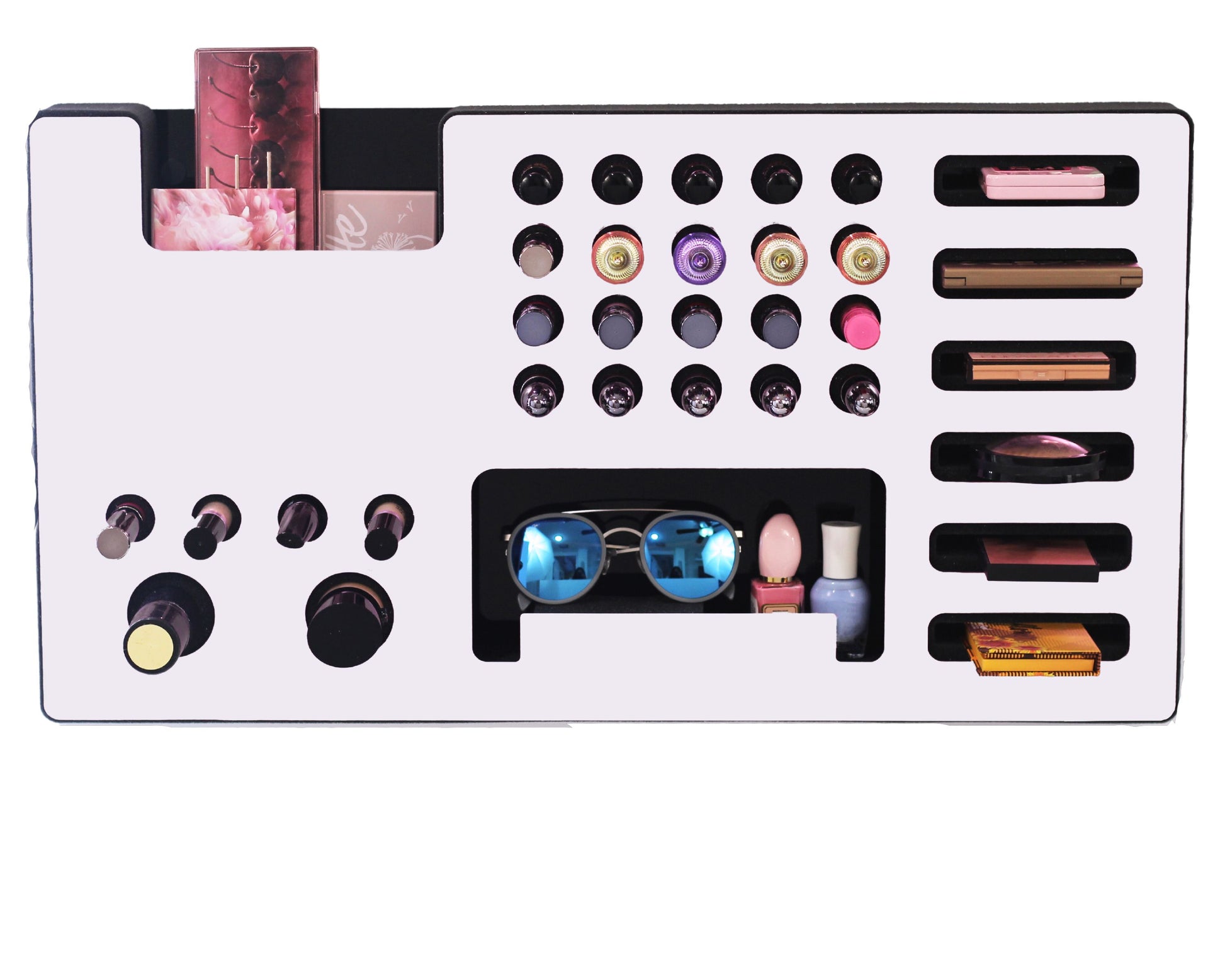 White Ultra Complete Makeup Solution Organizer shown mounted on the wall holding lipsticks, lip glosses, nail polishes, brushes, sunglasses and more by keeping items accessible and off of the counter. Shown next to a makeup vanity with samples of suggested items the organizer can hold. Shown with a white background.
